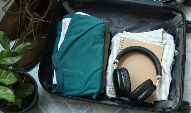 Close up of a person getting ready for travel and packing clothes into an open black suitcase, vacation travel concept. Person preparing for a trip and folding clothes into an open luggage.