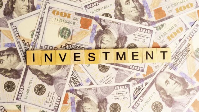 Wooden blocks spelling out the word investment positioned carefully on top of a scattered pile of American dollar bills
