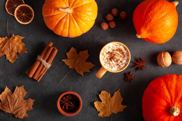 Seasonal top view composition with pumpkins, cinnamon, anise stars, nuts and a cozy cup of spiced coffee with whipped cream, creating perfect autumn atmosphere.