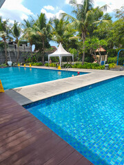 Tropical outdoor swimming pool surrounded by lush palm trees under bright sunny sky, creating a relaxing vacation atmosphere.