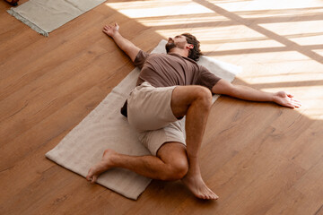 Yoga instructor performing reclining spinal twist on mat in studio