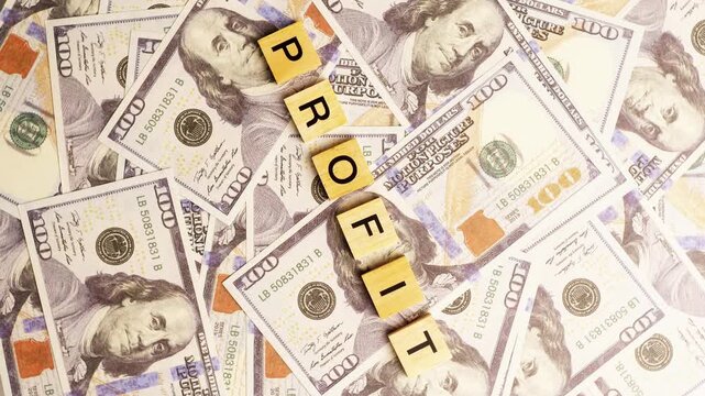 Wooden blocks spelling out the word profit resting on a flat pile of one hundred dollar bill paper currency