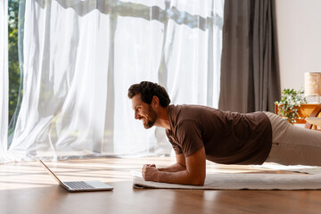 Man doing plank exercise at home watching online fitness class on laptop