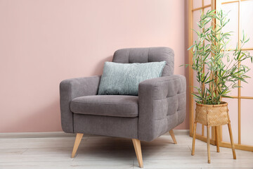 Comfortable armchair with cushion and houseplant near beige wall indoors
