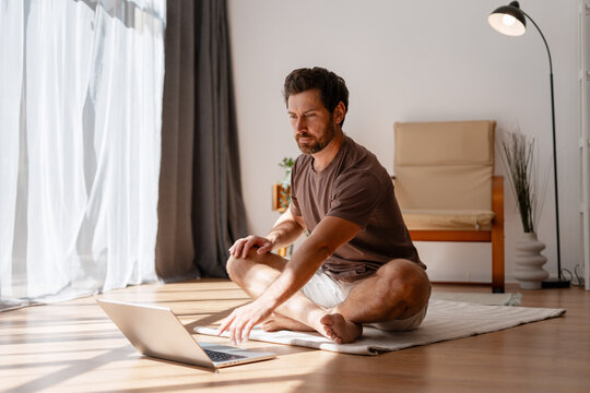 Man practicing yoga and working with laptop at home