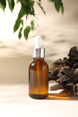 Promotion. Bottle of cosmetic product, green leaves and driftwood on beige background, closeup
