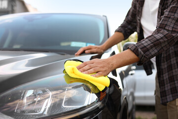 Man wiping car with yellow microfiber rag outdoors, closeup