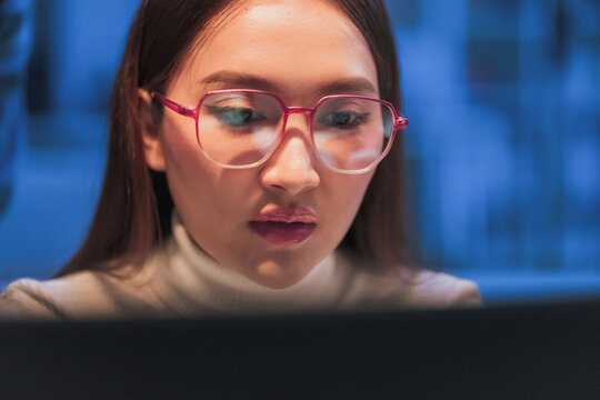 Asian programmer with glasses works late night shift in modern office, coding AI data analysis with artificial intelligence assistance for innovative tech solutions and machine learning development