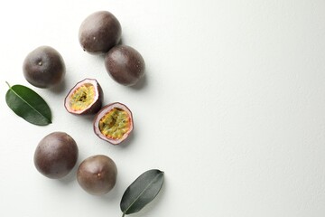 Fresh passion fruits with green leaves on white table, flat lay. Space for text
