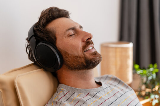 Man relaxing on armchair listening to music with headphones