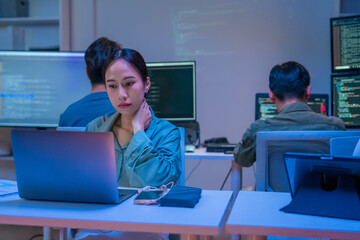 dedicated Asian businesswoman works late into the night in a dark modern office, focused on her...