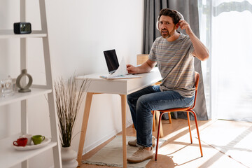 Confused businessman having a video call and adjusting headphones at home