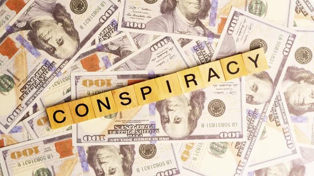 Wooden blocks spelling out the word conspiracy resting on a pile of one hundred dollar bills in a flat lay