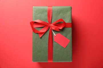 Gift box with blank tag on red background, top view
