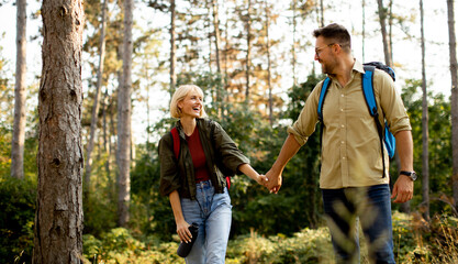 Happy couple hiking through a forest trail while holding hands in the bright sunlight during a warm afternoon