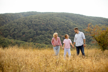 Family enjoys a walk in a golden field during autumn near a dense forest under a bright sky