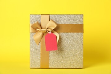 Gift box with blank tag on yellow background
