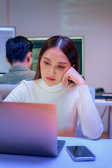 dedicated Asian businesswoman works late into the night in a dark modern office, focused on her...