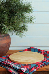 Empty round wooden chopping board on plaid napkin with christmas pine branches in clay pot