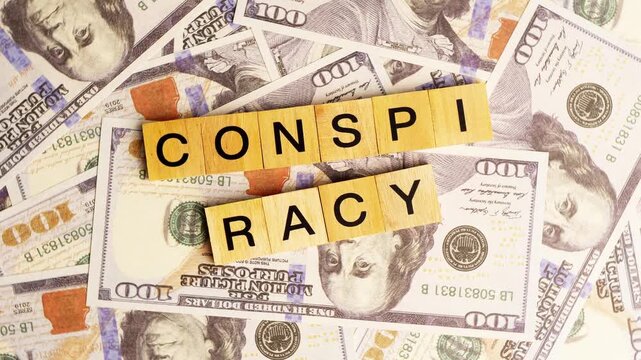 Wooden blocks with the letters "Conspiracy" arranged on a slowly rotating stack of dollar bills. Looping 360-degree of wooden blocks with the words "Conspiracy" as a business financial concept. 