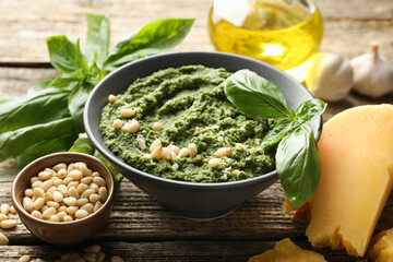 Fresh pesto sauce in bowl and ingredients on wooden table, closeup