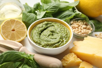 Fresh pesto sauce in bowl, ingredients and squeezer on table, closeup