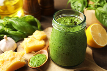 Fresh pesto sauce in jar and ingredients on table, closeup