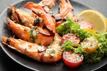 Tasty grilled shrimps served with salad and lemon on black table, closeup. Delicious seafood dish