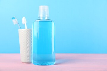 Mouthwash and toothbrushes on pink wooden table against blue background, space for text. Oral hygiene