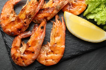 Tasty grilled shrimps with lemon and lettuce on black table, flat lay. Delicious seafood dish