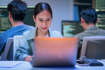 dedicated Asian businesswoman works late into the night in a dark modern office, focused on her...