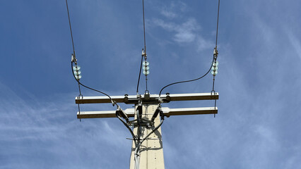 Electrical power lines and glass insulators on a concrete utility pole against a blue sky