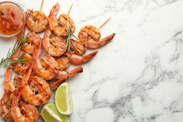 Skewers with tasty grilled shrimps, lime slices, herbs and sauce on white marble table, flat lay with space for text. Delicious seafood dish