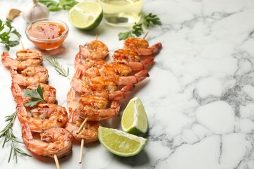 Skewers with tasty grilled shrimps, lime slices, herbs and sauce on white marble table, closeup with space for text. Delicious seafood dish