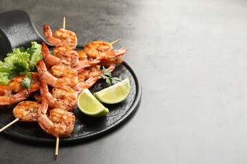 Skewers with tasty grilled shrimps, lime slices, parsley and lettuce on grey table, space for text. Delicious seafood dish