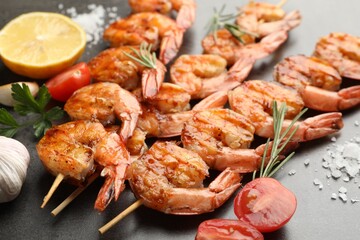 Skewers with tasty grilled shrimps, tomatoes and spices on grey table, closeup. Delicious seafood dish