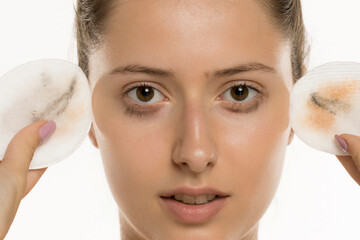 Studio shot of young woman closeup face holding used cotton pads with removed makeup on white...