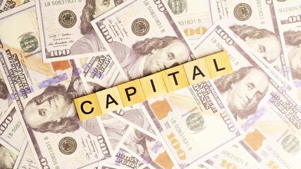 Wooden blocks with the letters "Capital" arranged on a slowly rotating stack of dollar bills. Looping 360-degree of wooden blocks with the words "Capital" as a business financial concept. 4K footage.