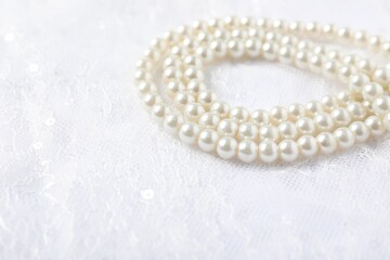 Beautiful pearl necklace on lace fabric, closeup. Space for text