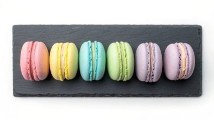 Six pastel colored macarons arranged in a row on a dark slate platter