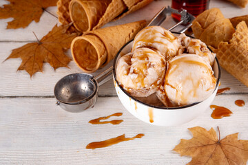 Tasty fall season maple syrup ice cream. Bowl with maple syrup taste gelato, with a lot of syrup drizzles on top, with maple leaves and ice cream cones on table, copy space