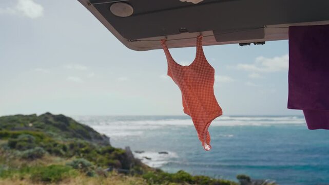 A vibrant orange swimsuit is drying by the coast with waves crashing against the shore
