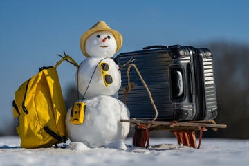 Snowman with sunglasses and backpack. Funny snowman holding suitcase on snowy trip. Christmas...