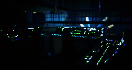Obraz premium The control room is filled with illuminated screens displaying various data in a dark setting. The ambient blue and green lights create an electronic atmosphere, suggesting high tech activity.