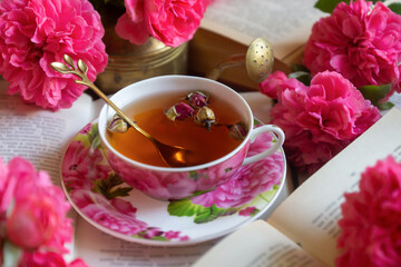 A cup of aromatic tea, a book and a rose on the table.