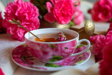 A cup of aromatic tea, a book and a rose on the table.