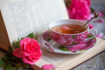 A cup of aromatic tea, a book and a rose on the table.