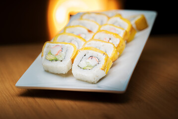 A row of sushi rolls with a yellow outer layer, likely tamago. The rolls, filled with crab and avocado, are on a white plate with a warm, glowing background