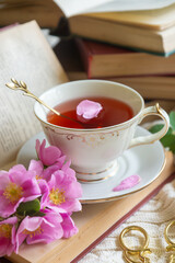 A cup of aromatic tea, a book and a rose on the table.
