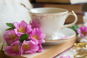 A cup of aromatic tea, a book and a rose on the table.